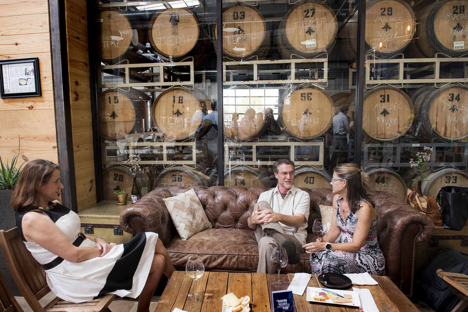 People on a leather sofa in front of a rack of wine casks